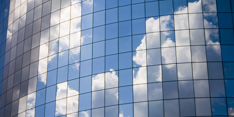 Close-up of blue sky and clouds reflected in windows of an office building.