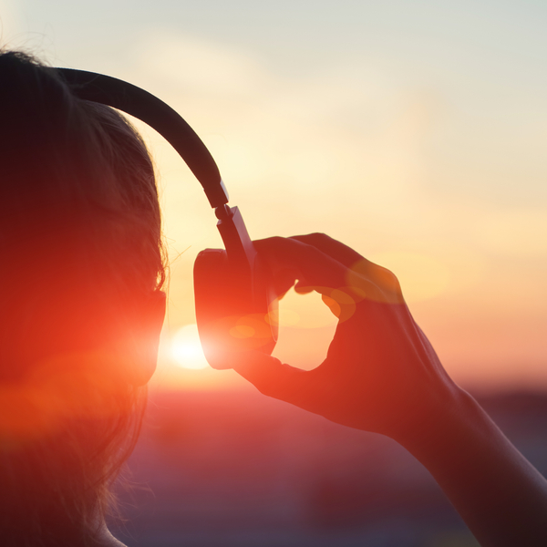 Close-up of woman wearing headphones with sun in background.