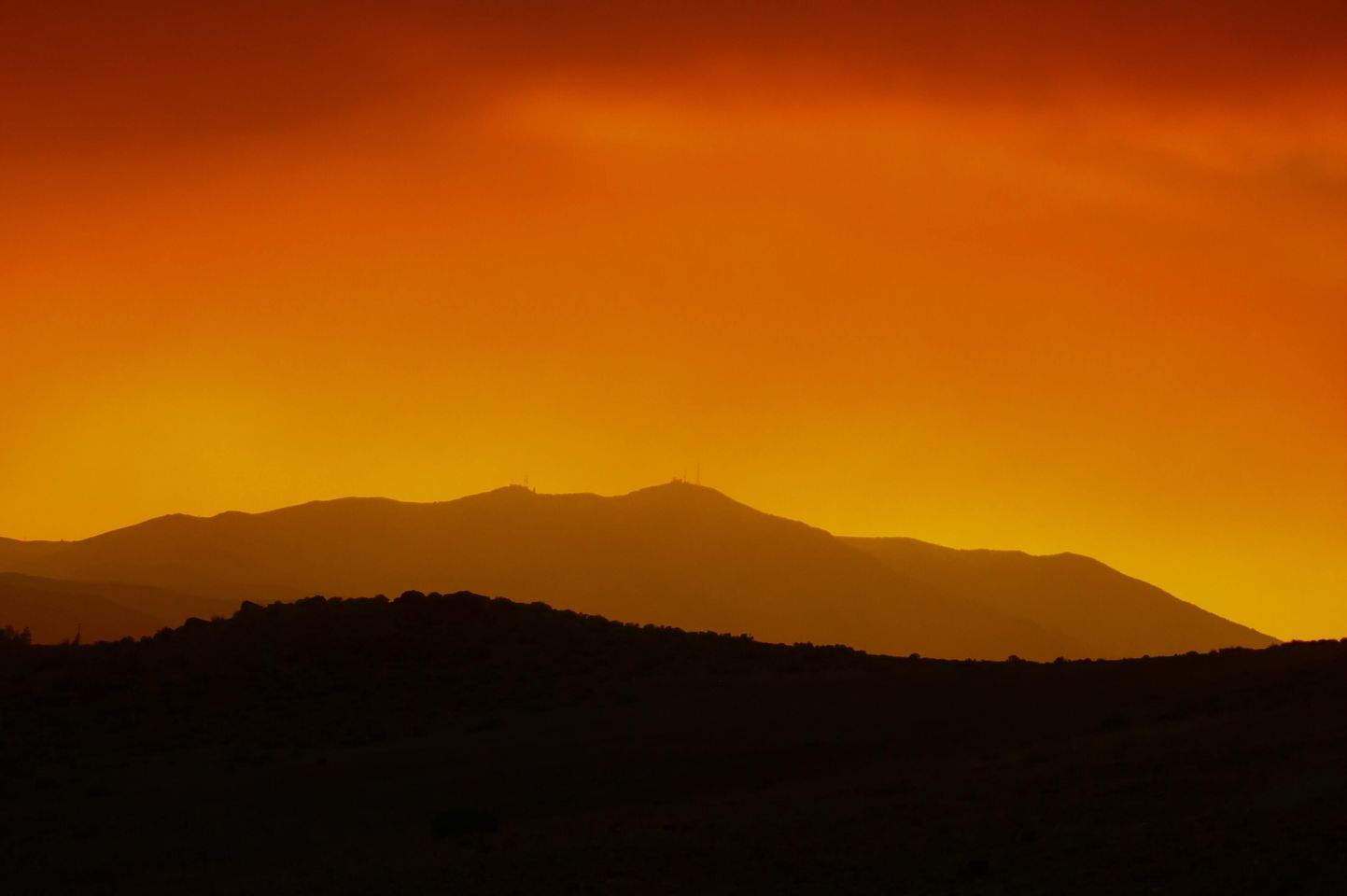 Wide angle of mountain range silhouetted against orange sky.