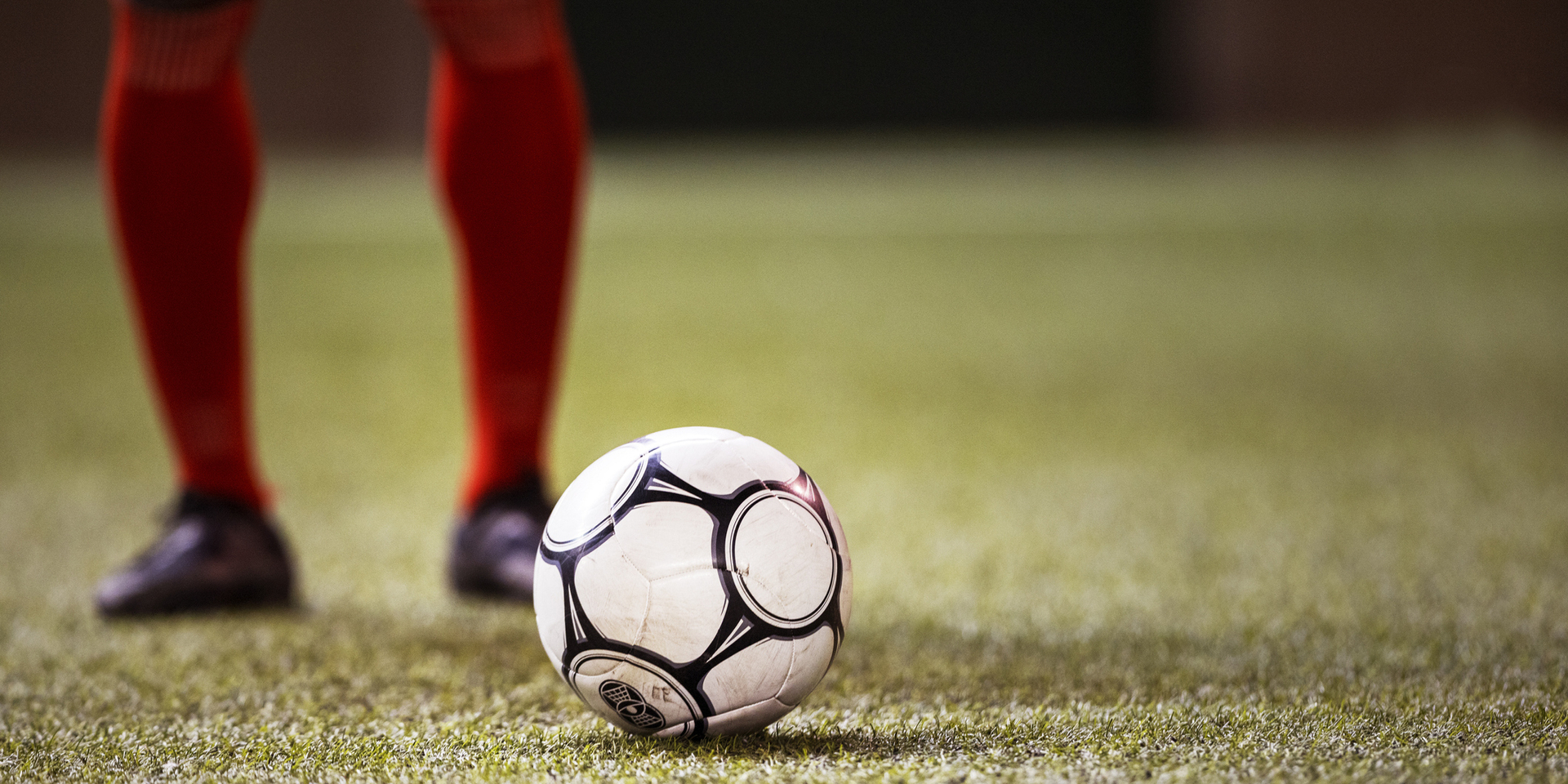 International football player wearing shin guards and cleats positions himself behind a soccer ball on a grass field in big athletic stadium and prepares to kick off professional championship game