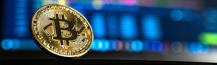 Close-up of gold bitcoin with computer screen blurred in the background.