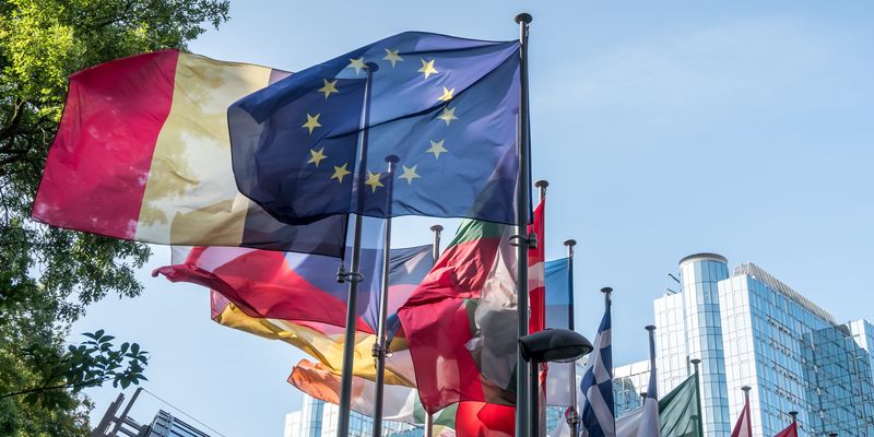 Up angle of European Union and various European national flags in front of the Paul Henri Spaak European Parliament building in Brussels, Belgium.