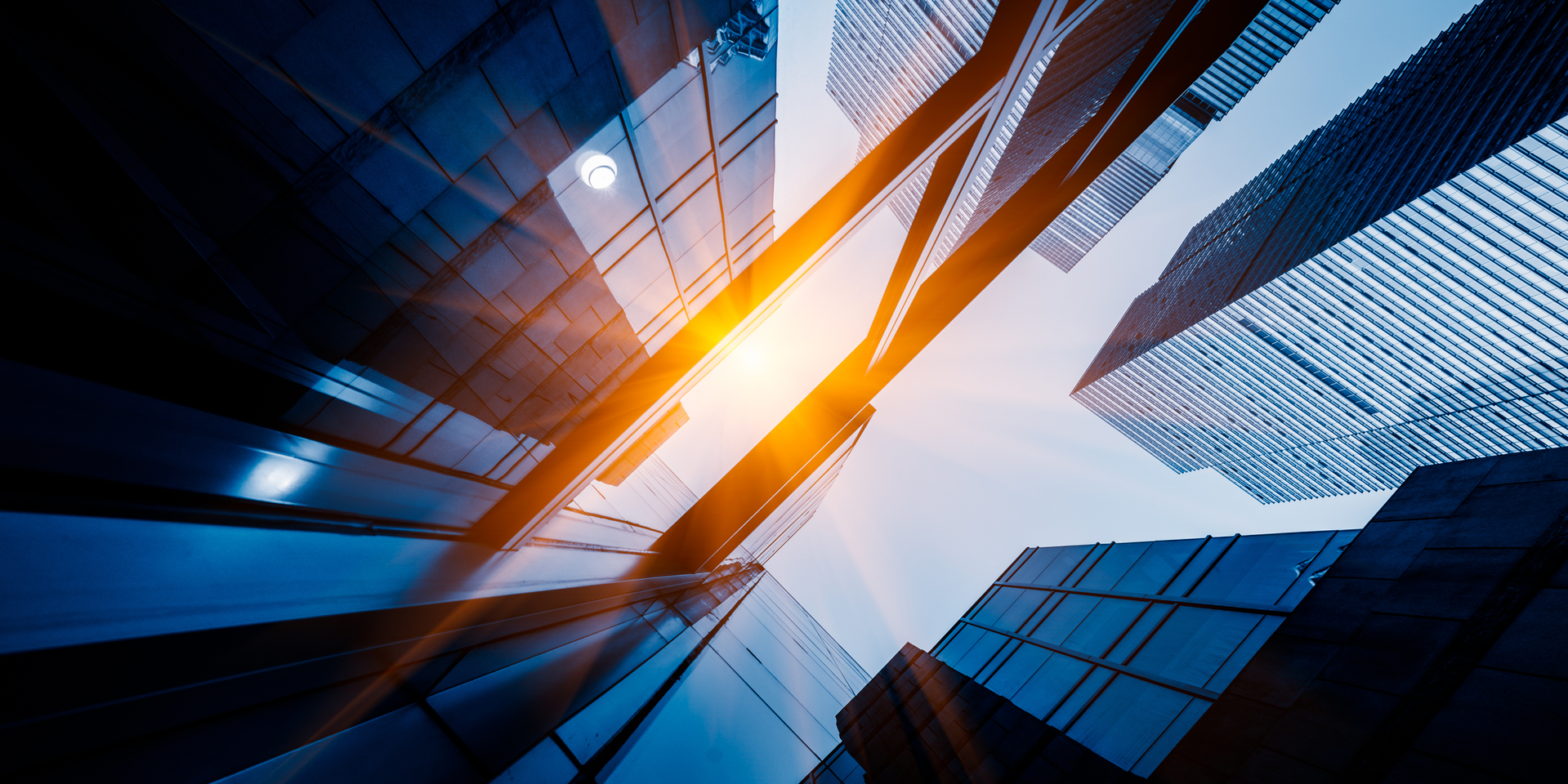 Up angle of multi-story glass office buildings with sun reflecting off glass.