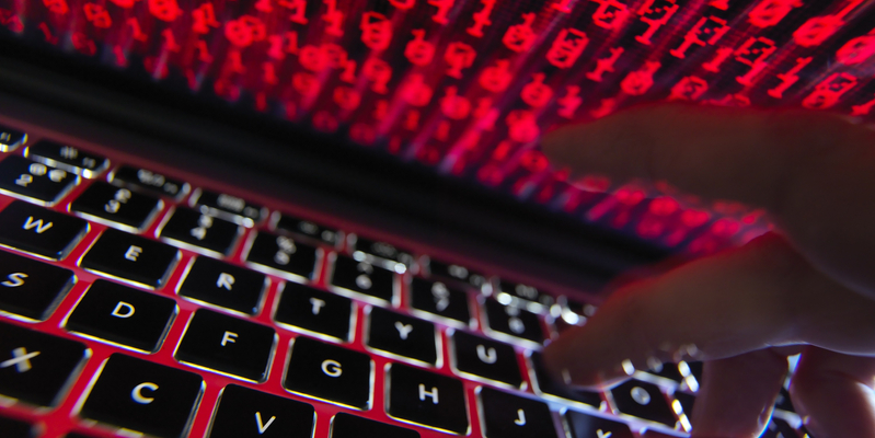 Close-up of fingers typing on laptop keyboard with binary code on computer monitor.